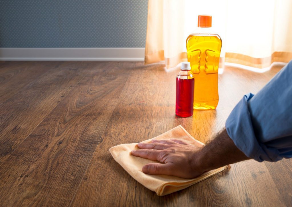 A person's hand cleans a hardwood floor with a soft cloth. two bottles of cleaning solution sit nearby.