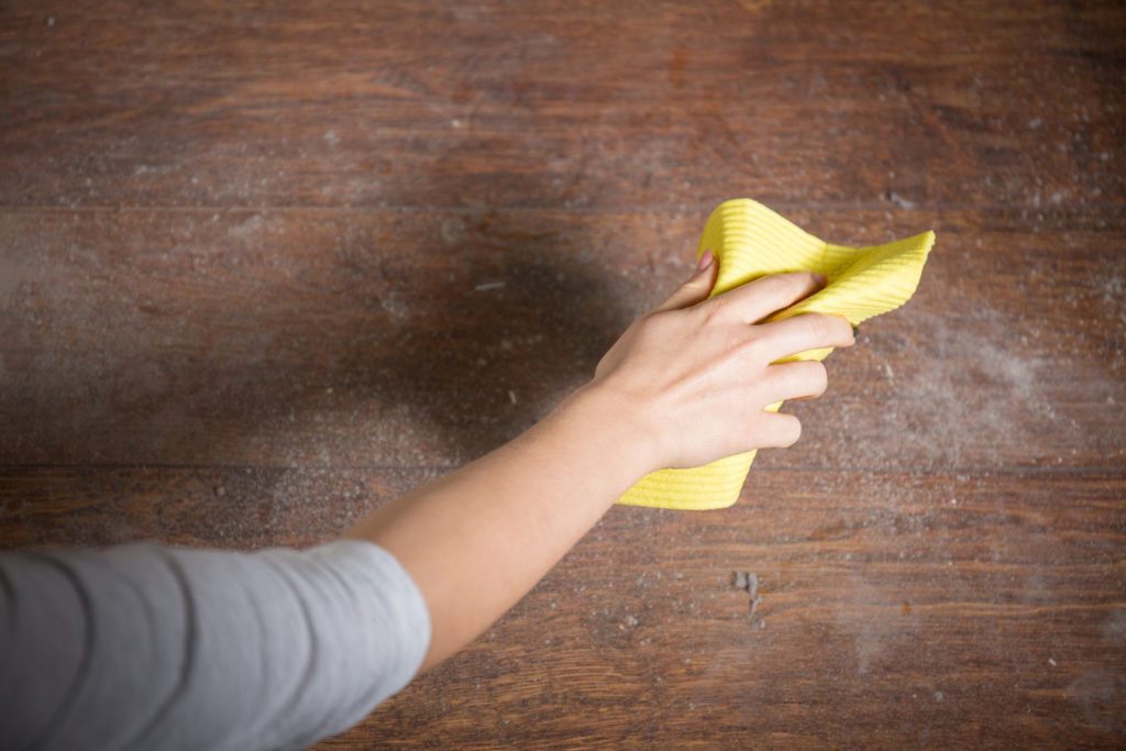 A person cleans a dusty parquet floor with a microfiber cloth.