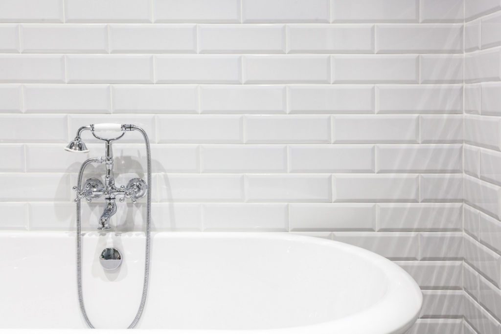A wall of white porcelain bathroom tiles around a bathtub.