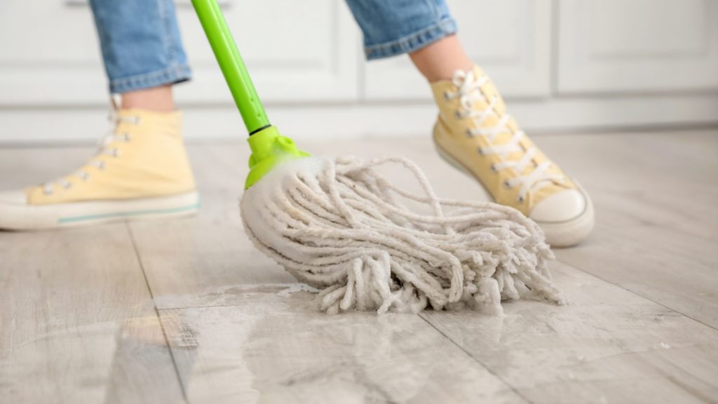 A homeowner wearing yellow sneakers cleans her kitchen tile